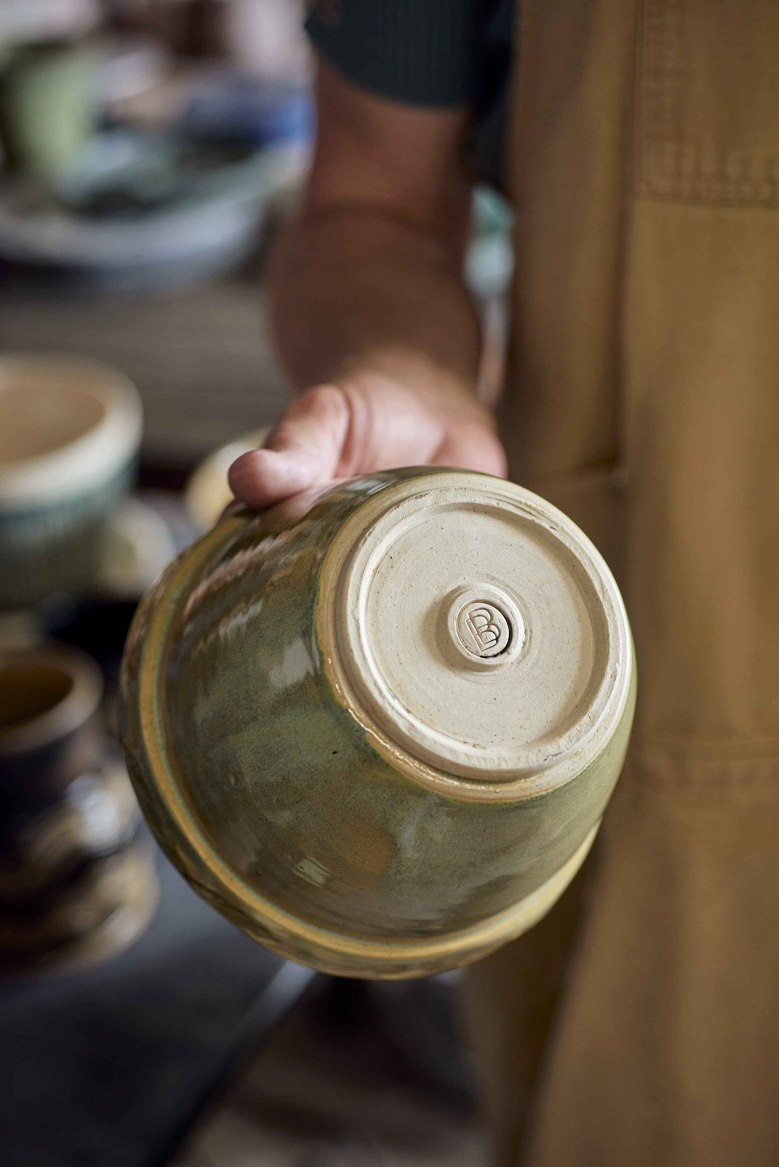 Person holding a ceramic pot with Brian Burgess Ceramics logo. with a blurred background
