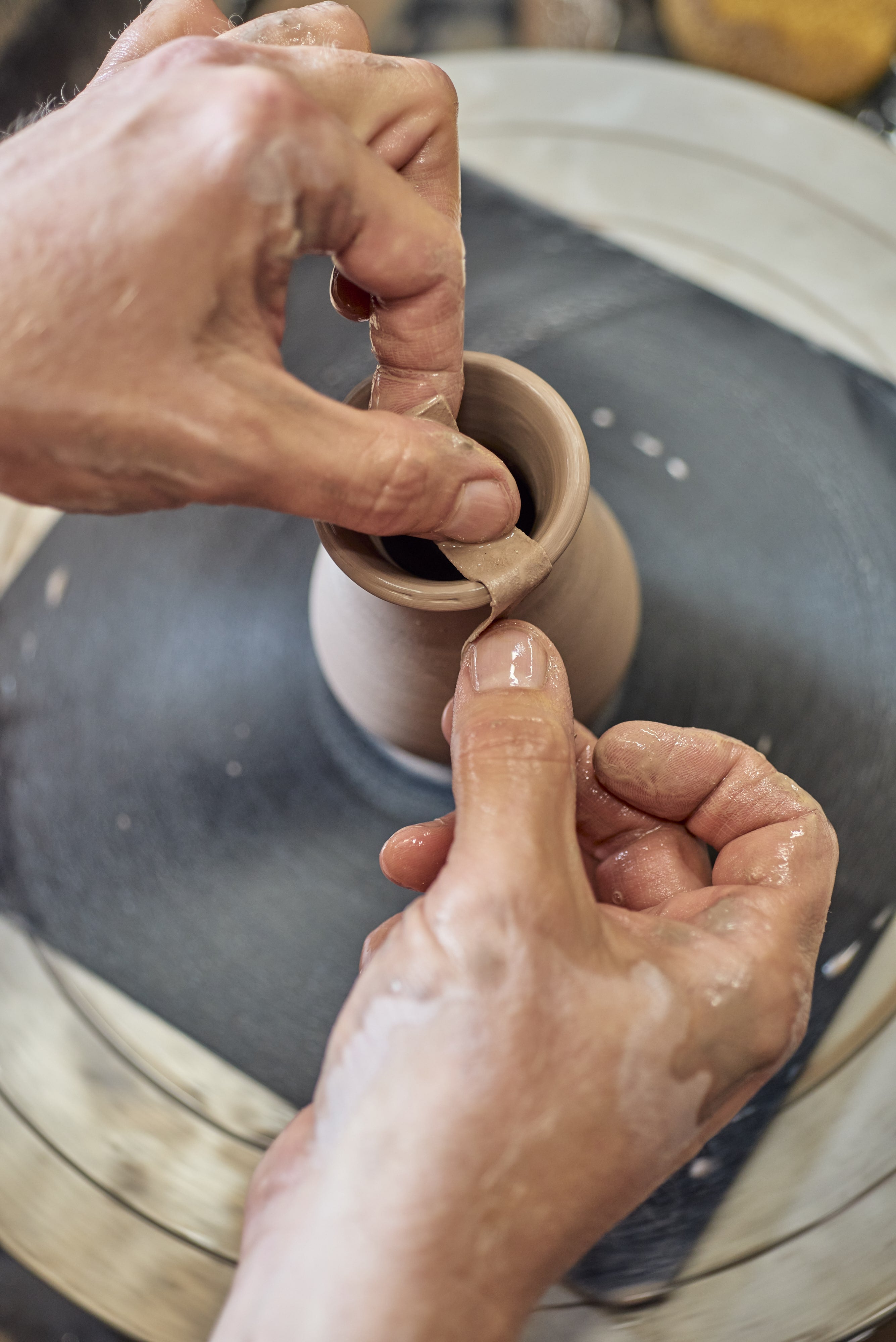 Close-up of hands working on a potter's wheel with a clay piece.
