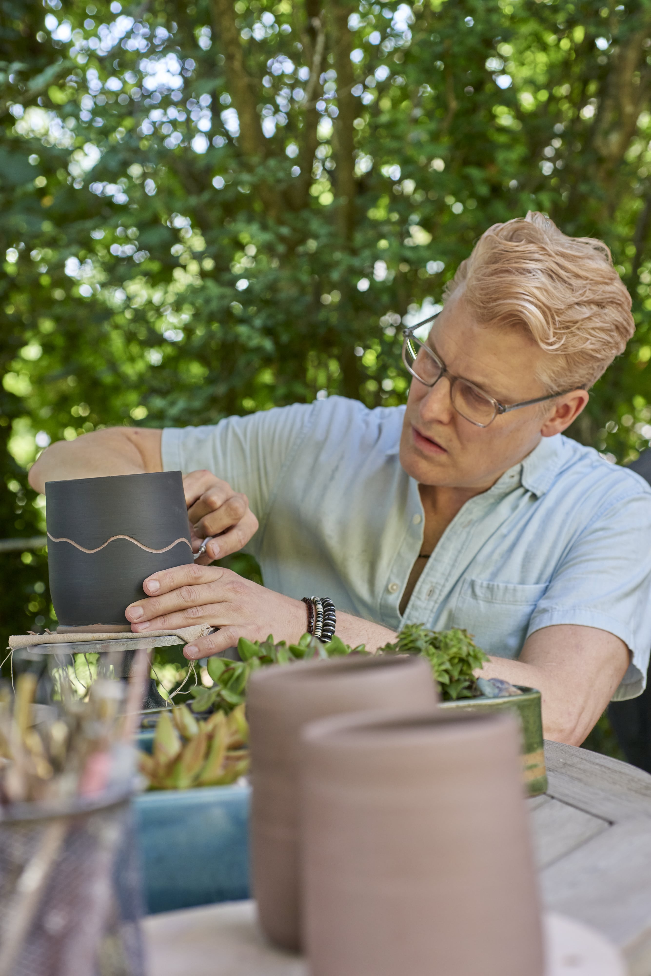 Brian creating molding on a piece of pattery outside surrounded by greenery