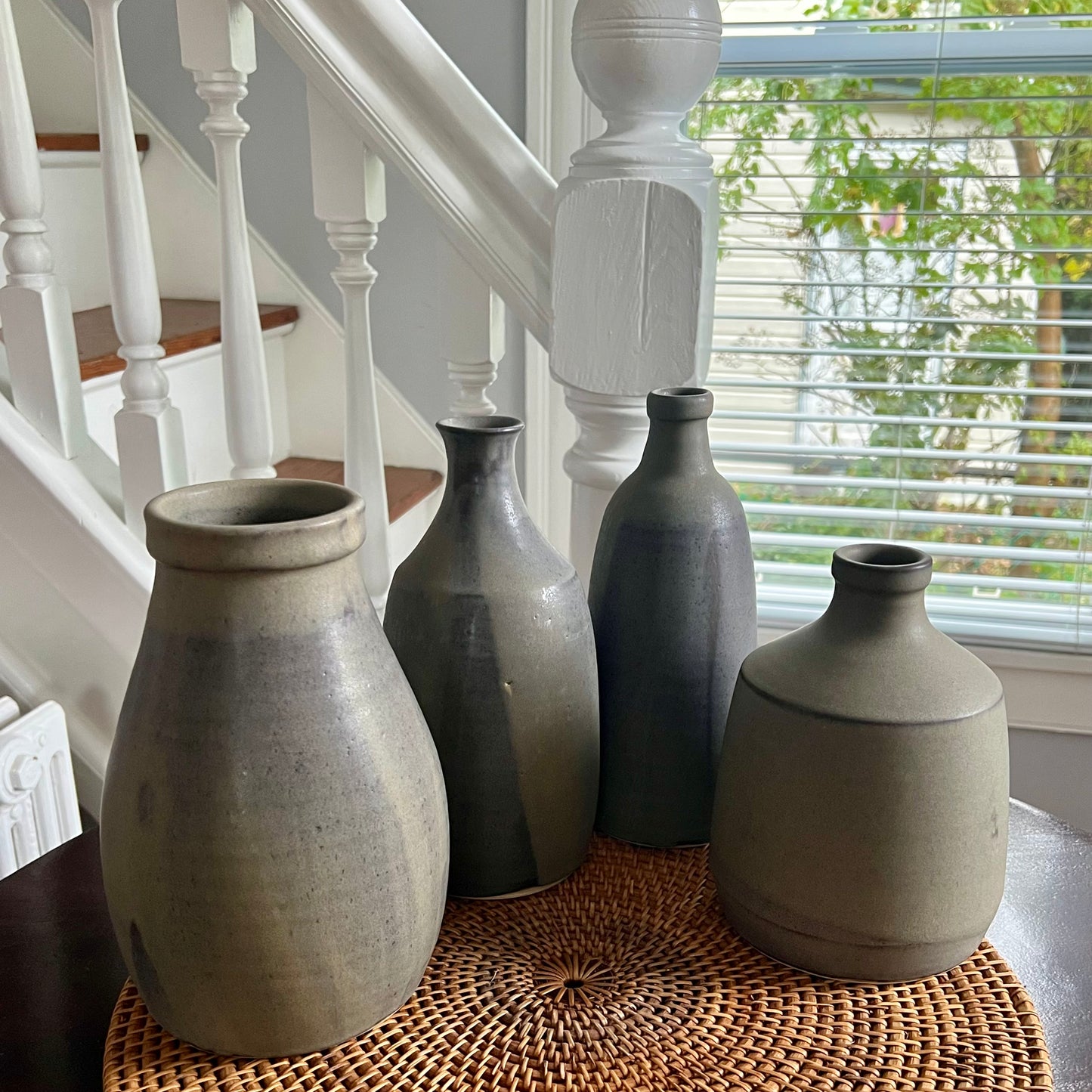 Plump, squat bottle. Finished in pour-over pussywillow (brown/gray matte glaze). Image of four vases of different shapes and sizes set on table.