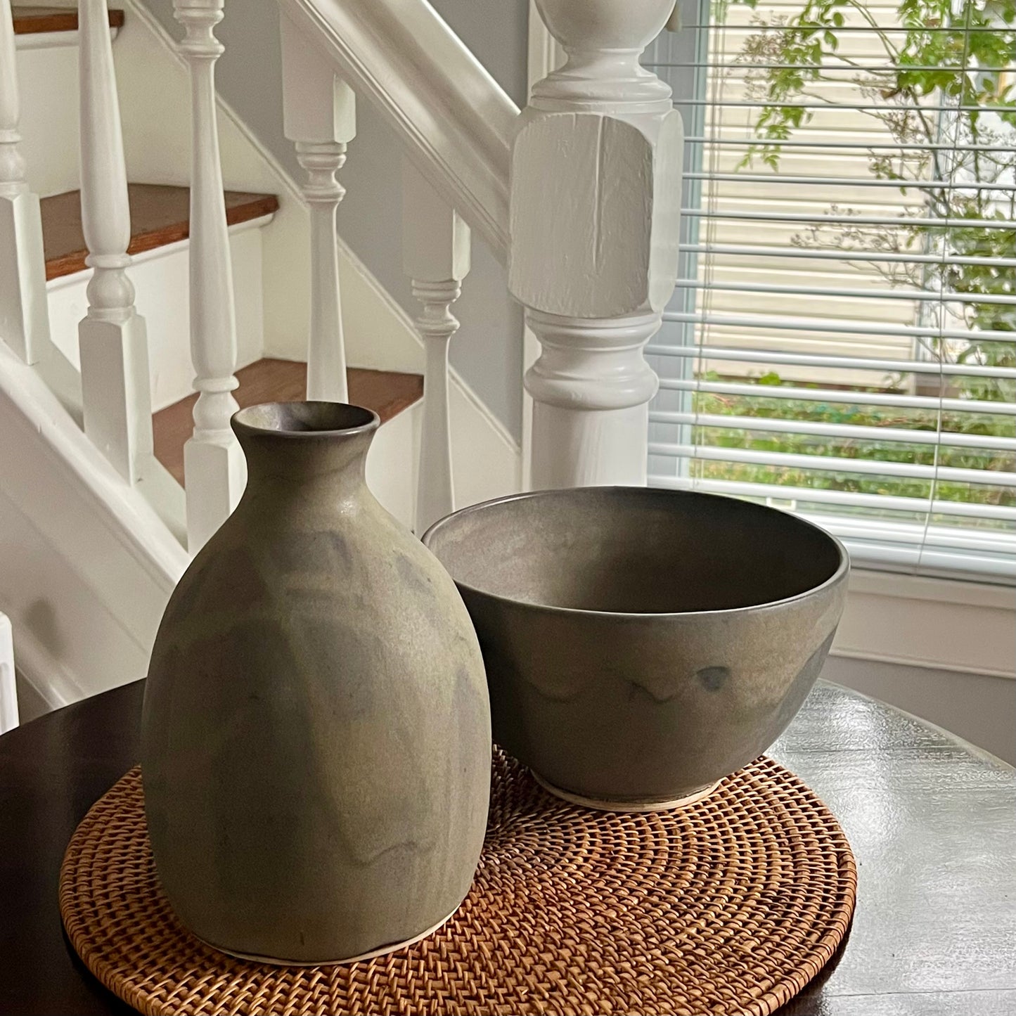 Wide body jug that works as a vase as well as a decorative piece. Finished in pussywillow (a gorgeous gray/brown matte finish). Image of jug and bowl set on table.